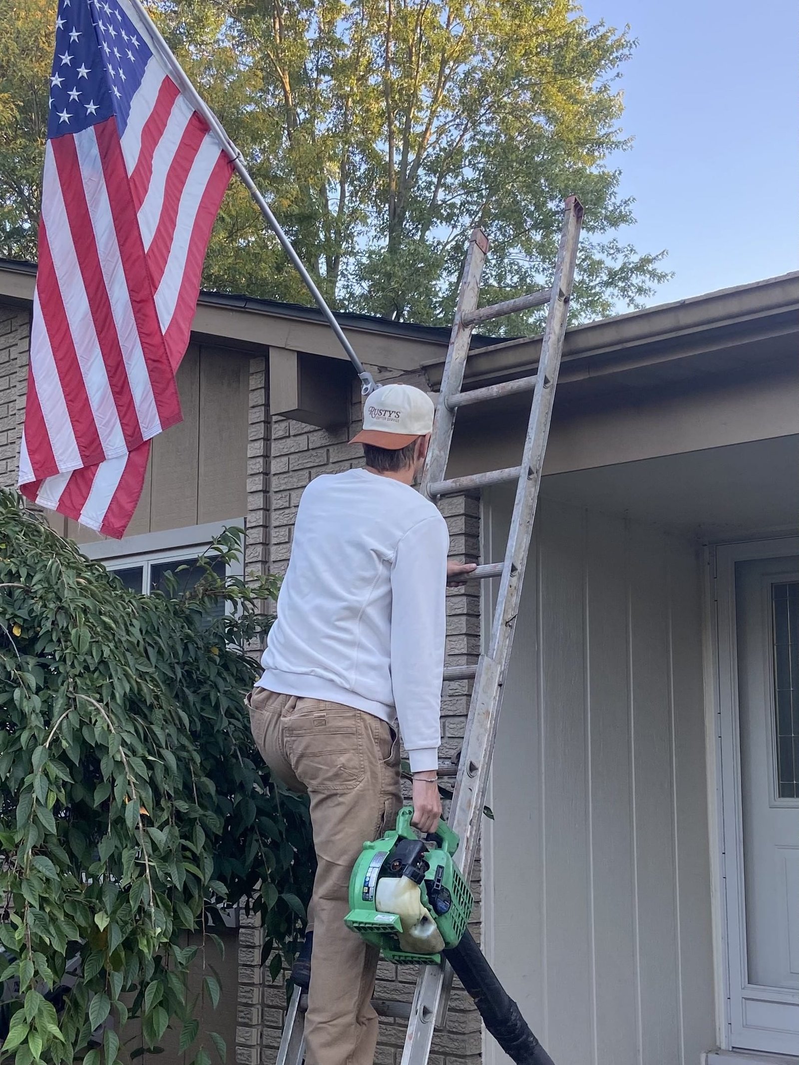 Rustys_Gutter_Service man climbing ladder to clean gutters